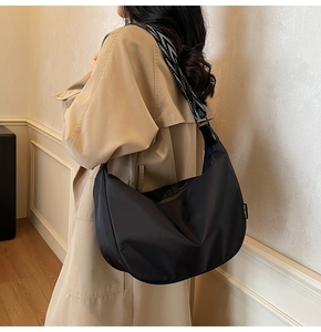 Detail of black Hobo bag with geometric jacquard strap worn with a beige trench coat