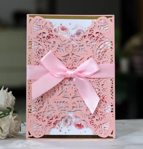Detail of pink laser-cut wedding invitation with satin bow and pearl finish texture