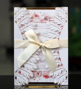 Detailed close-up of white laser-cut feather lace wedding invitation with beige silk ribbon
