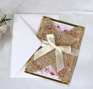 Detail of laser-cut floral invitation cover with champagne gold finish and cream bow