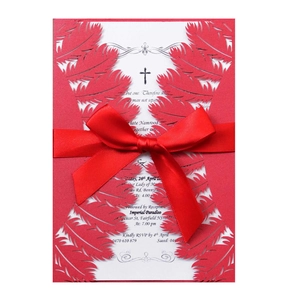 Macro shot of laser-cut red feather wedding invitation with white card and red ribbon bow