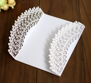Detailed laser-cut white wedding invitation card with lace heart patterns on wood