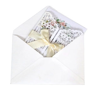 Detailed laser-cut wedding invitation featuring white lace patterns and a cream satin bow