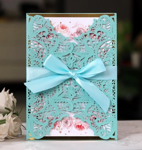 Detail of laser-cut turquoise invitation with a blue satin ribbon and floral insert card