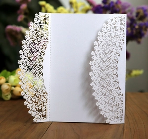 Elegant white laser-cut wedding invitation with floral lace patterns on a wooden table