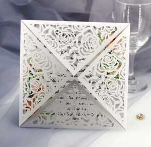 Macro shot of white laser-cut wedding invitation featuring elegant rose floral patterns
