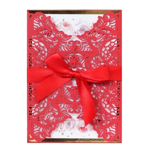 Macro shot of laser-cut red wedding invitation with floral insert and satin ribbon bow