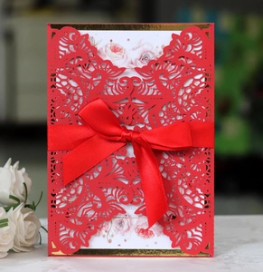 Close-up of laser cut floral wedding invitation with red ribbon bow and white inner card
