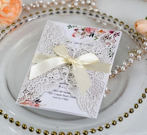 Detail of laser-cut lace wedding invitation with a cream ribbon bow and floral inner card