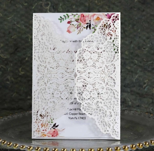 Close-up of laser-cut lace wedding invitation with floral insert on a glass tray