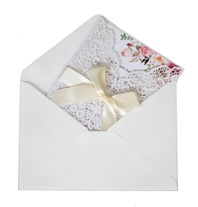 Close-up of laser-cut white wedding invitation with floral insert and cream ribbon bow