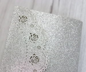 Intricate laser-cut silver glitter wedding invitation card with rose floral pattern