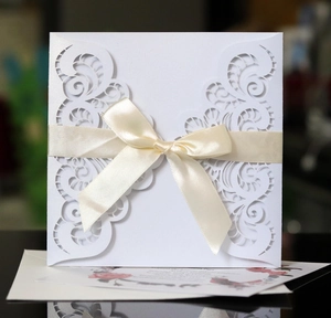 Elegant white laser-cut wedding invitation featuring a cream silk bow and floral insert