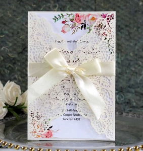 Detail of laser-cut lace wedding invitation with ribbon bow on a glass tray