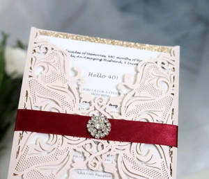 Detail of pink laser-cut invitation with red satin ribbon and rhinestone buckle