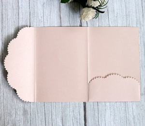 Light pink pearlescent laser-cut tri-fold wedding invitation on a rustic wood surface