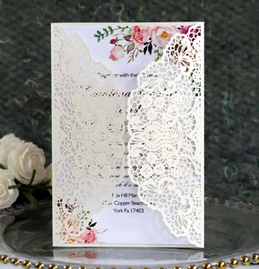 Detailed laser-cut lace wedding invitation set on a decorative silver tray background