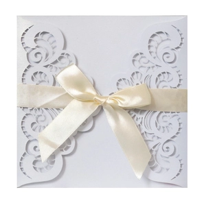 Close-up of laser cut hollow pattern with ribbon bow on white wedding invitation card