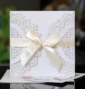Detailed close-up of white laser-cut floral wedding invitation card with ivory ribbon bow