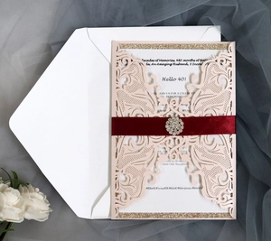 Detail of laser-cut nude invitation card featuring a burgundy ribbon and rhinestone brooch