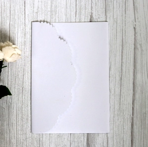 Close-up of white laser-cut invitation envelope with floral edge on wood background