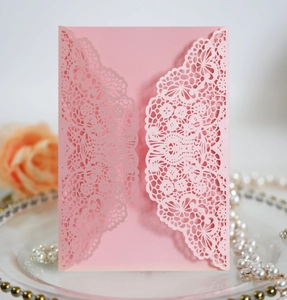 Detail of pink laser cut wedding invitation card with lace floral design and pearlescent finish