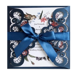 Detail of laser-cut navy blue wedding invitation with intricate scrollwork and satin ribbon