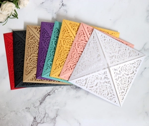 Detailed laser-cut rose hollow invitation cards in multiple colors on white marble