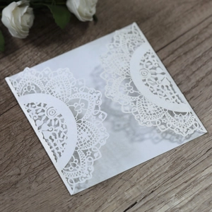 Close-up of white laser-cut lace invitation envelope on a vintage wooden table