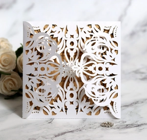 Detail of white laser cut hollow wedding invitation with elegant gold insert and floral pattern