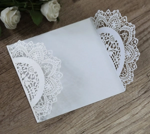 Macro detail of white laser-cut floral wedding invitations on a light wooden table