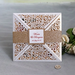 Close-up of laser cut wedding invitation with floral patterns and a gold glitter belly band