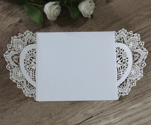 Close-up of white laser-cut wedding invitation featuring intricate lace rose patterns