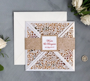 Detail of laser cut floral wedding invitation with champagne glitter band and white envelope