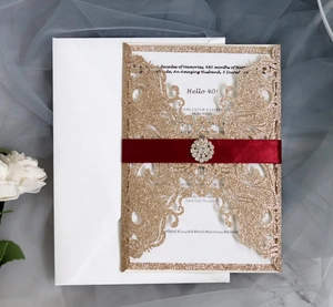 Dettaglio dell'invito tagliato al laser con glitter, nastro rosso e fibbia in strass
