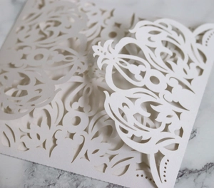 Close-up of white laser-cut floral lace wedding invitation with detailed paper texture