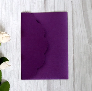Detail of dark purple wedding invitation with laser-cut wave edges on wood background