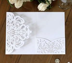 Elegant white laser-cut floral invitation card on dark wood table with roses decoration