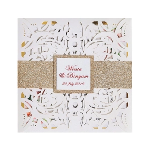Detail of laser-cut wedding invitation with white floral patterns and gold glitter band