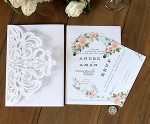 Elegant white laser-cut floral wedding invitation set with pink floral card on wood