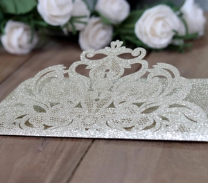 Détail d'invitation de mariage argentée pailletée avec découpe laser et motifs floraux