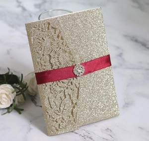 Detail of glitter gold laser-cut invitation with burgundy ribbon and rhinestone buckle