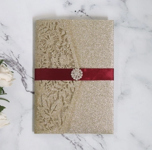 Detail of laser-cut gold glitter invitation featuring red satin ribbon and rhinestone brooch