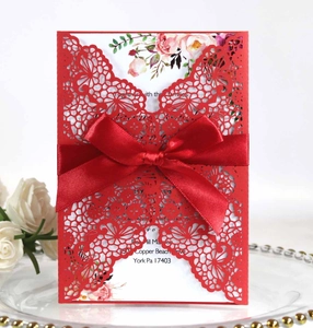 Detailed laser-cut red wedding invitation with floral insert and elegant ribbon bow