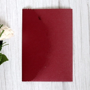 Detail of burgundy laser-cut invitation cover on wood background with white flower