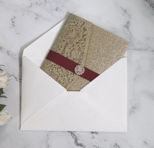 Close-up of laser-cut glitter gold sunflower invitation with burgundy ribbon and rhinestone