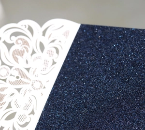 Détail macro du motif floral découpé au laser sur papier pailleté bleu foncé pour invitations