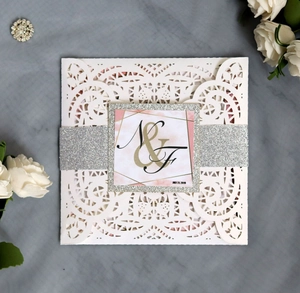 Close-up of laser-cut lace wedding invitation with silver glitter band and custom letters
