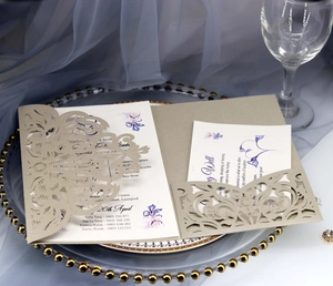 Detail of laser-cut grey invitation sleeve with floral inner card on elegant tableware