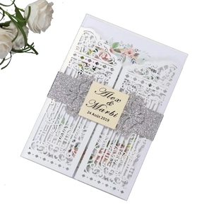 Close-up of laser-cut white wedding invitation with glitter band and floral liner